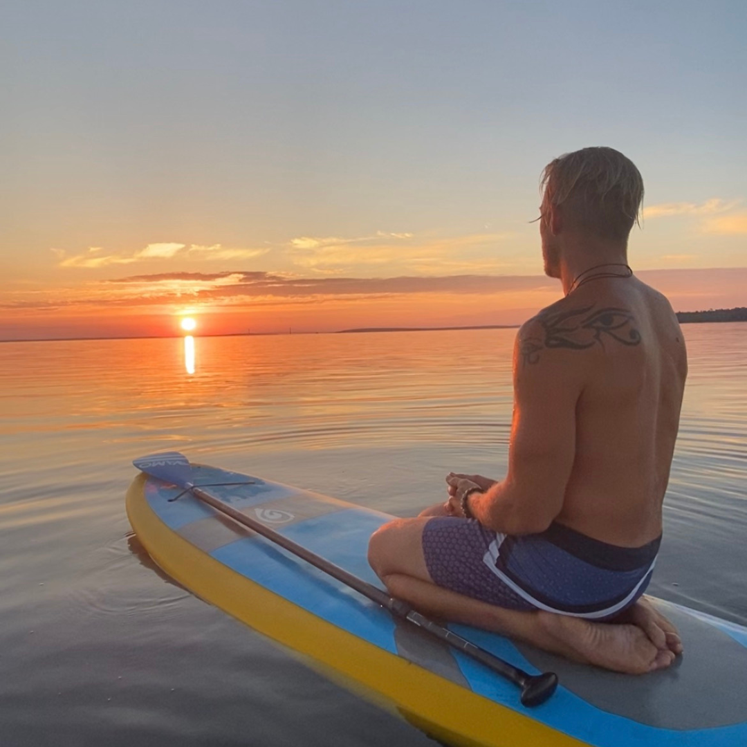 male kneeling on paddle board watching sunset